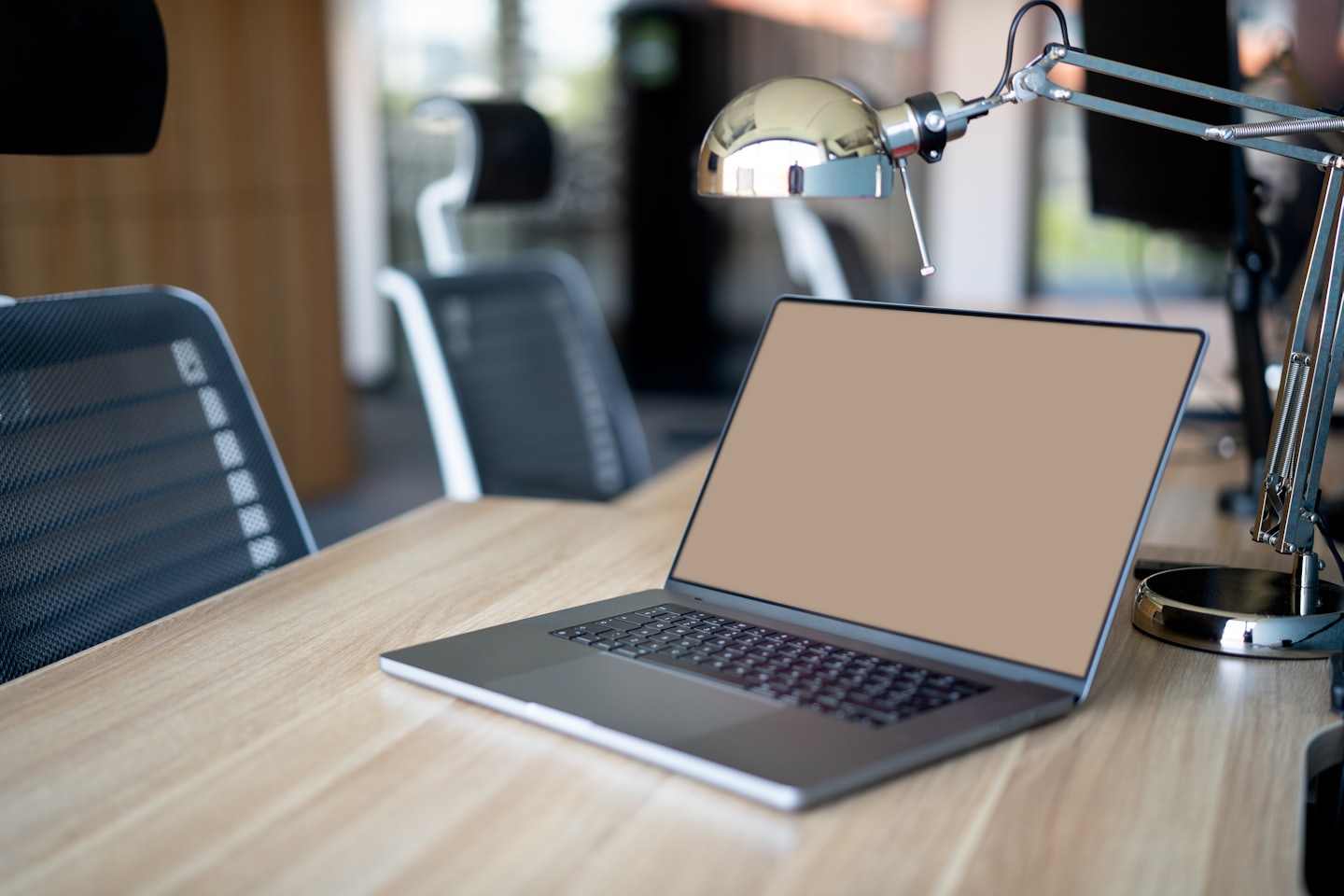 A modern laptop sits on a light wooden desk.