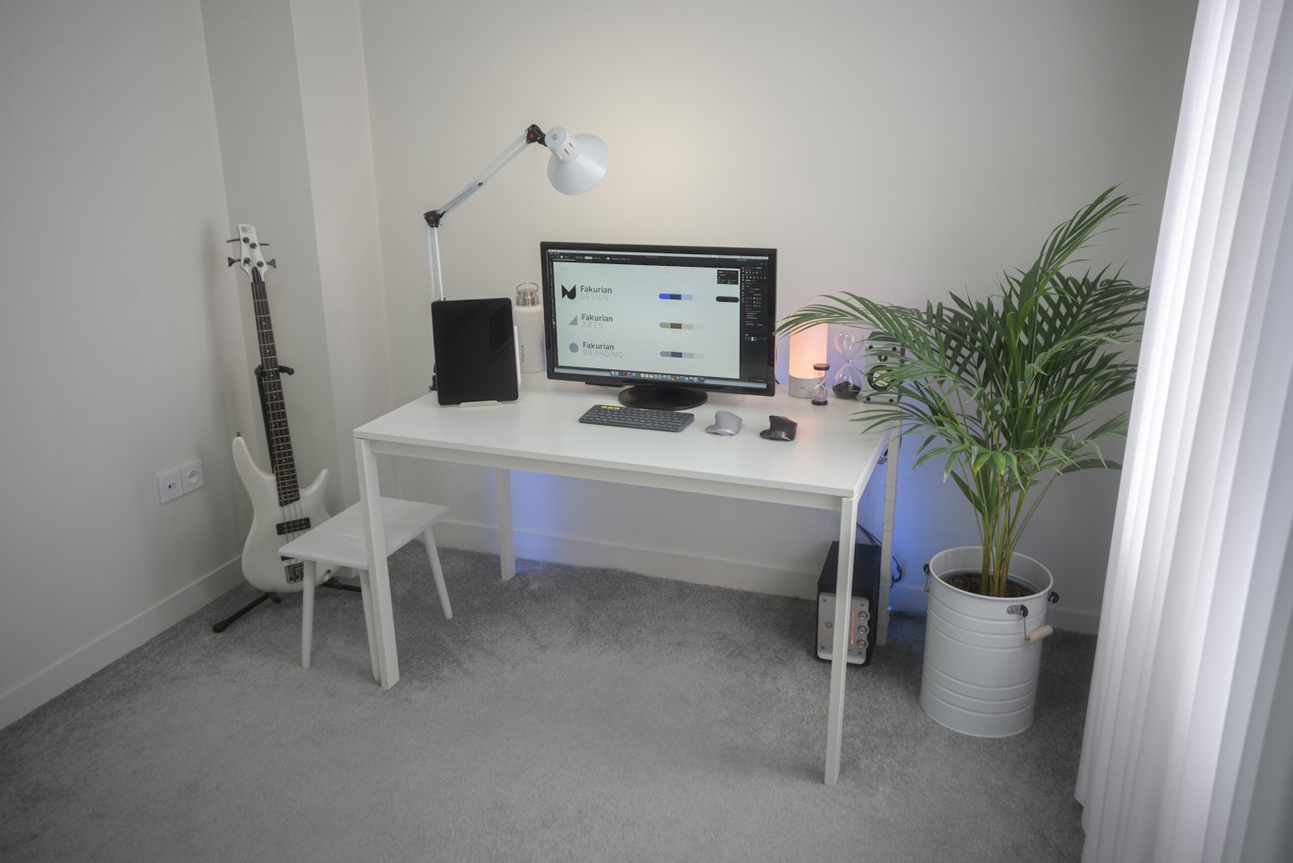 Modern home office with computer, tablet, and bass guitar.